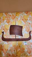 Wooden sail boat art mounted on wall with floral wallpaper background.