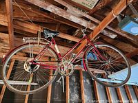 Side view of vintage red TECHNIS bicycle hanging, showing overall frame, tires, saddle and rear rack.