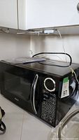 Full view of black Philips microwave sitting on counter under cupboards. Visible power cord. Reflective door and silver handle.