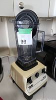 Full view of the blender showing the clear pitcher with handle and black lid on a beige base with controls and brand name.
