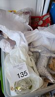 Plastic storage bin containing clear glass Christmas ornaments wrapped in tissue paper and a silver glitter reindeer figurine, with a red decorative box visible in the background.
