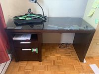 Full view of the dark brown office desk showing the glass top and drawer unit on the left side.