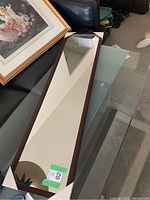 Full view of rectangular full body mirror with dark wood frame resting on a glass table showing clean reflective surface and frame details.