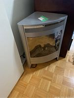 Mini electric fireplace corner unit shown from an angle, displaying the curved glass front and artificial logs inside.