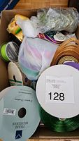 Box containing a variety of ribbon spools, including green satin, gold, and decorative ribbons.