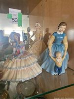 Three Royal Doulton porcelain figurines displayed in glass cabinet, showing the colorful and detailed hand-painted designs on the figures.