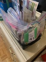 Photo showing a black basket on a dresser containing multiple resealable plastic bags filled with assorted sticker sheets with various colorful shapes and patterns.