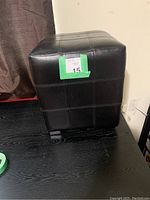 Single brown vegan leather footstool showing stitched pattern and cube shape, labeled with lot number.