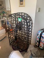 Front view of tall black metal wine rack with arched top and detailed scrollwork, showing doors closed.