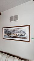 Wall-mounted framed artwork showing a winter landscape with bare trees and snowy ground under a calm sky.