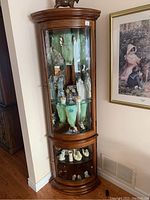 Front view of wooden corner curio cabinet with curved glass door and decorative top.