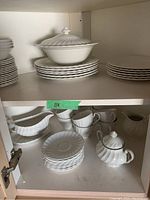 White porcelain dinnerware set with plates, bowls, cups, covered serving dish, teapot, creamer, and gravy boat inside cabinet.