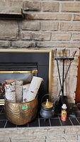 Wide shot of the fireplace hearth with brass log holder containing birch logs, black kettle, can of FireMagic Cleaner, and black metal tool stand with tools.
