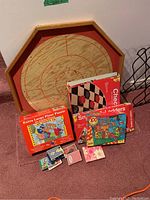 Photo showing wooden shuffleboard board, floor puzzle box, two boxed board games (Checkers and Snakes & Ladders), and multiple decks of playing cards in front of them.