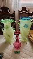 Overview of three decorative glass vases displayed together: two tall uranium glass vases and one small cranberry glass vase