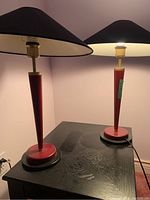 Pair of red and black matching table lamps on a black wooden table against a light wall background.