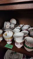 Wide view of assorted floral porcelain tea cups and plates stacked and grouped on a shelf
