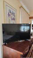 Front view of Samsung 32-inch flat screen TV on wooden cabinet under floral artwork.