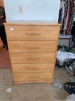 Front view of the tall wood dresser showing five closed drawers with horizontal wooden handles and a smooth top.