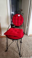 Front view showing black wrought iron frame and red tufted cushions on vanity chair.