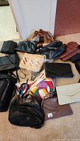 Collection of vintage women's purses and clutches spread on floor, showing variety of colors, materials, and styles