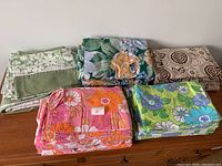 View of all five vintage bedding pieces arranged on a surface showing variety of floral and geometric patterns.