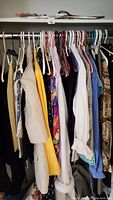Womens clothes on hangers showing a variety of blazers, tops, and dresses in multiple colors and patterns.