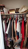 Photo showing a closet rod filled with various women's clothing items including shirts, tops, blazers, and dresses in multiple colors and patterns.