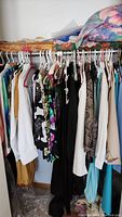 Clothes hanging on a rack showing various colors and styles including black, floral, white, and beige shirts and dresses.