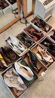 Top view showing nine pairs of women's shoes in boxes arranged on carpet including glittery silver slingbacks, brown peep-toe heels, and more.