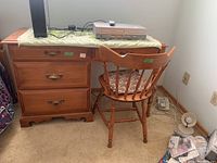 Wood desk with three drawers, a decorative cloth on top, and a matching chair with a floral seat cushion.