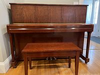 Upright piano with matching bench in front, showing closed key cover and wood finish.