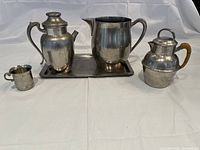 Photo showing the full set of five pewter pieces: tray, pitcher, two chocolate pots, and baby cup
