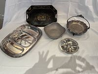 All metal serving pieces displayed together on white cloth background showcasing variety and condition.
