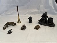 Overview of entire lot showing metal statue, dinner bell horn, and various animal figurines on a white fabric backdrop