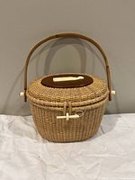 Angled front view of Nantucket basket purse with handle upright, showcasing the woven design, dark wooden lid inset, and ivory toggle closure.