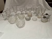 Full view of the lot showing two lamps, various goblets, small plates, creamer, sugar container, and serving pieces arranged on a white cloth.