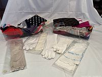 Two plastic bins showing multiple scarves in an assortment of patterns and colors, white gloves, and small woven cross-body bags.