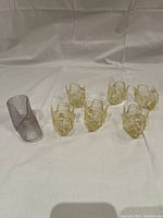Photo showing six yellow swan-shaped finger bowls arranged with one clear glass baby bootie figure on a plain light background.