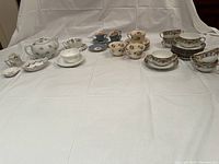 Wide view showing the full collection of tea cups, saucers, teapot, honey pot, and tea bag holders spread on a white cloth.