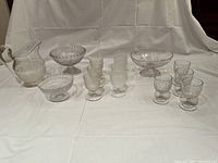 Wide shot showing the pressed glass pitcher, three footed bowls, and ten goblets arranged on a white cloth background.