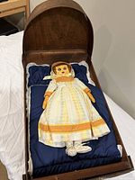 Wooden doll bed with leather doll dressed in white and yellow-orange dress laying inside