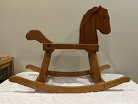 Side view of wooden rocking horse showing horse head, seat, curved runners, and tail handle.
