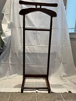 Front view of the dark wood suit valet stand with hanger and pants bar against a white backdrop