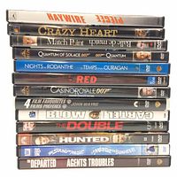 Stack of 14 DVDs showing spines with titles including Haywire, Crazy Heart, Match Point, Quantum of Solace 007, Nights in Rodanthe, Red, Casino Royale 007, Blow, The Double, The Hunted, The Sound of Music, The Departed, Agents Troubles, 4 Film Favourites John Wayne Collection.