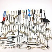 Full assortment of spoons, forks, knives, kitchen tools, and fishing lure laid out on flat surface