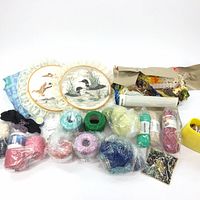 Overview of all items showing colorful spools of yarn, floss, buttons, and embroidery hoops with bird designs surrounded by lace.
