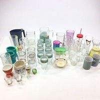 Wide view of all assorted glassware including tumblers, mugs, shot glasses, and pitcher arranged on white background