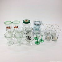 Overview of entire lot showing all glasses and jar, including Dos Equis beer glasses, parfait cups, Olympic torch glasses, champagne flutes, jar and others.