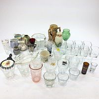 Full lot view showing assorted glassware including pitchers, mugs, clear glass votive holders, and decorative glass pieces.